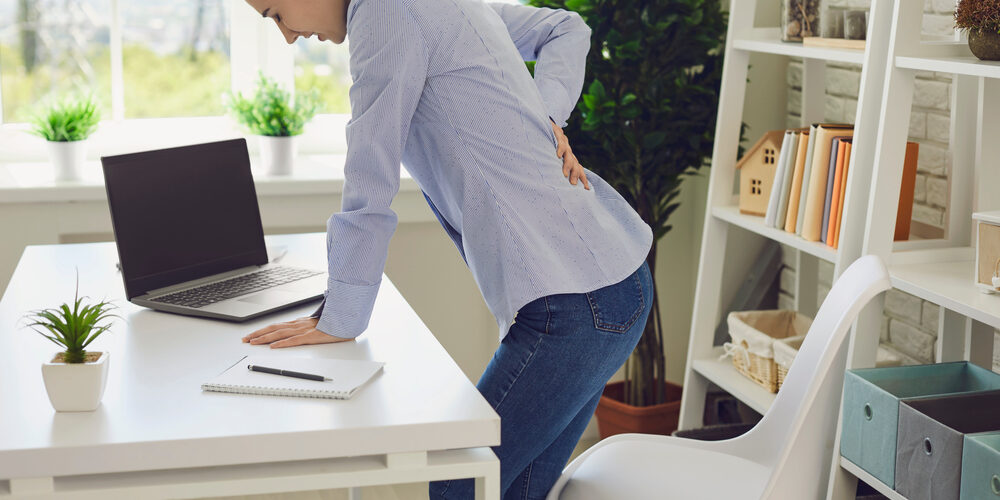 Woman experiencing lower back pain due to sciatica muscle spasm at her home office.