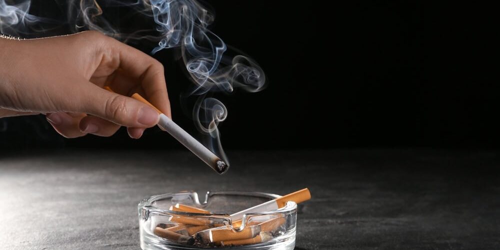 Hand dropping cigarette into ashtray with smoke, highlighting smoking's impact on spinal health.